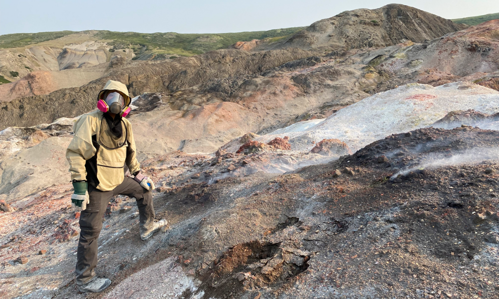 Un scientifique portant un masque respiratoire se tient debout sur un versant rocheux.