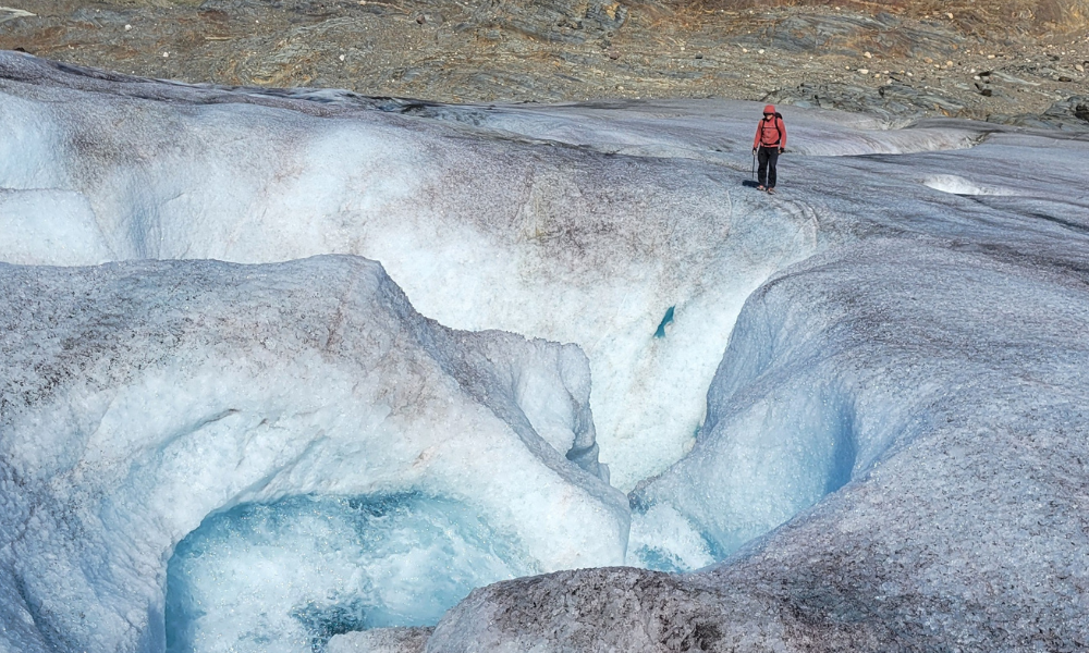 Un scientifique se tient au bord d’un immense trou dans un glacier.