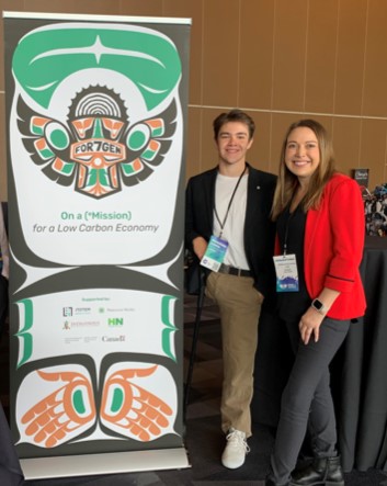 Deux personnes portant des cordons se tiennent debout à côté d’une affiche où est écrit&nbsp;: « On a (*Mission) for Low Carbon Economy. »