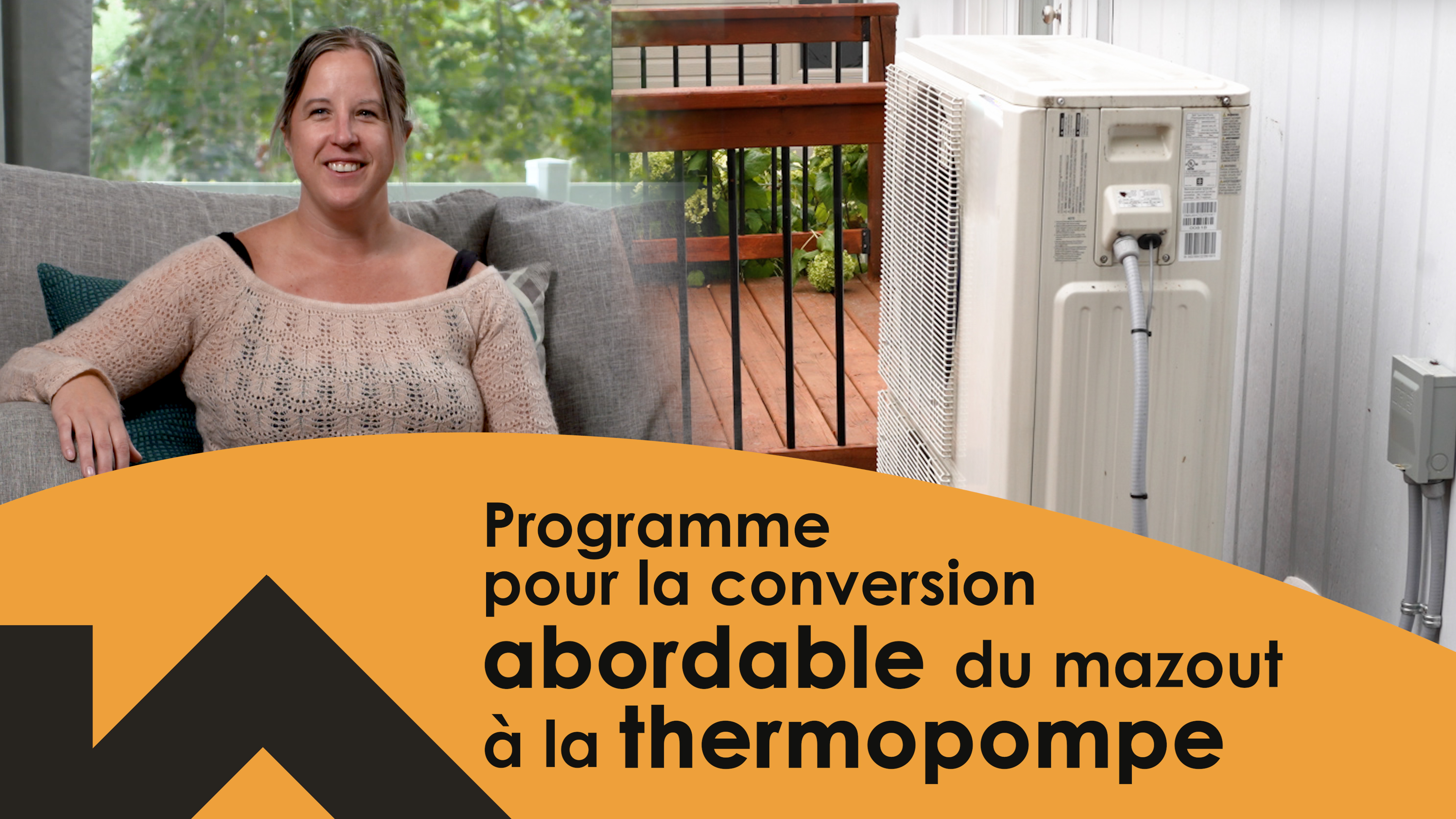Une femme souriante appuie son bras sur une thermopompes posée sur un support métallique à côté de sa maison.