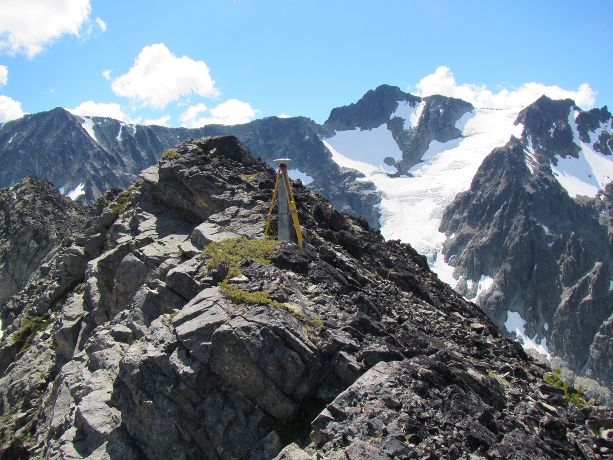 Un paysage montagneux de la frontière illustrant les opérations de terrain de la CFI, avec une borne et un trépied positionné sur un rocher alpin à découvert.