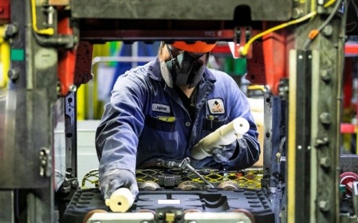 Une personne portant de l’équipement de protection utilise de la machinerie sur une chaîne de production industrielle.
